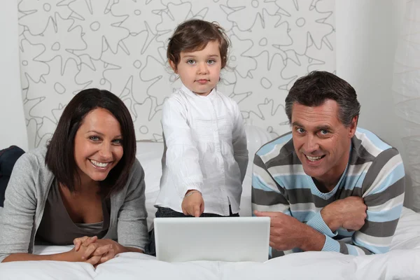 Föräldrar och dotter på sängen med dator — Stockfoto