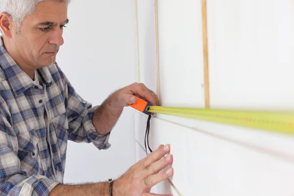 Grey haired handyman measuring wall — Stock Photo, Image