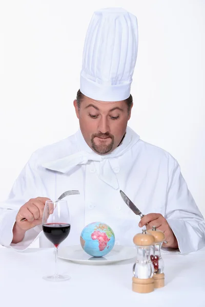 Повар-повар смотрит маленький глобус в тарелке — стоковое фото