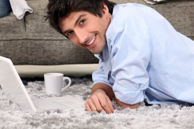 Man lying on carpet with coffee and computer clipart