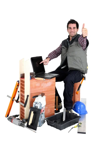 Thumbs up from a bricklayer with a laptop — Stockfoto