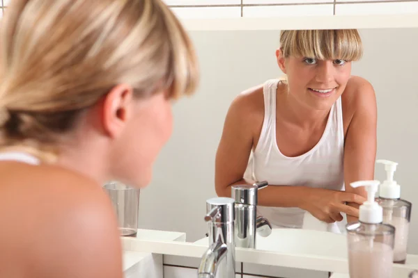 Młoda kobieta patrząca w lustro w łazience — Zdjęcie stockowe