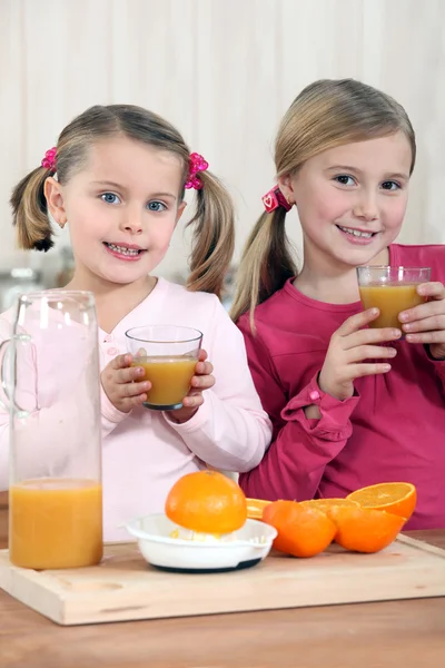 Dos chicas jóvenes bebiendo jugo de naranja fresco en la cocina — Foto de Stock