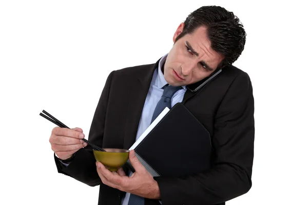 Бизнесмен ест японскую еду во время телефонной связи — стоковое фото