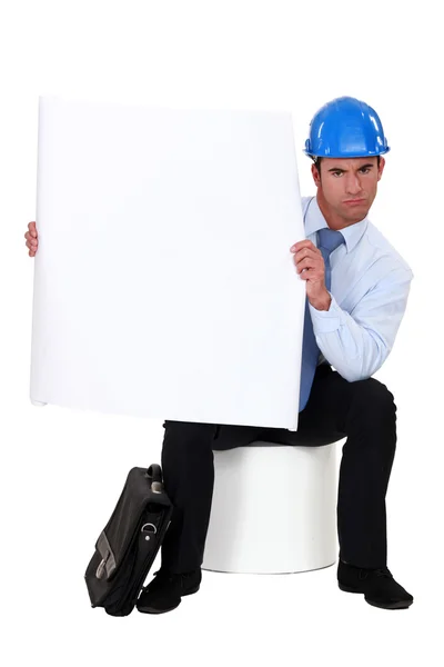 Homem de negócios com um capacete na cabeça segurando um cartaz em branco — Fotografia de Stock