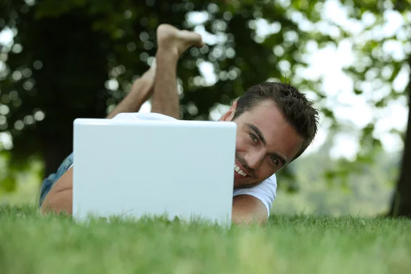 Homem usando seu laptop em um gramado — Fotografia de Stock