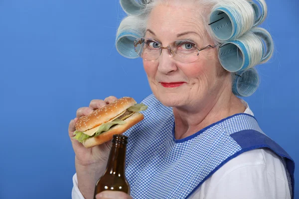 Abuela comiendo una hamburguesa y bebiendo una cerveza — Foto de Stock