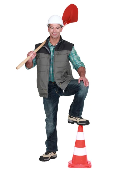 Trabalhador rodoviário segurando uma pá e apoiando o pé em um cone de tráfego — Fotografia de Stock