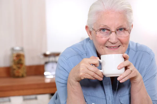 Пожилая дама наслаждается чашечкой чая на кухне — стоковое фото