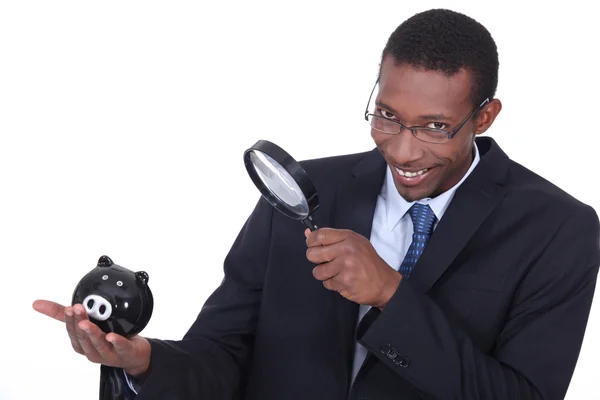 Afro-American businessman with piggy bank and magnifying glass — Stock Photo, Image