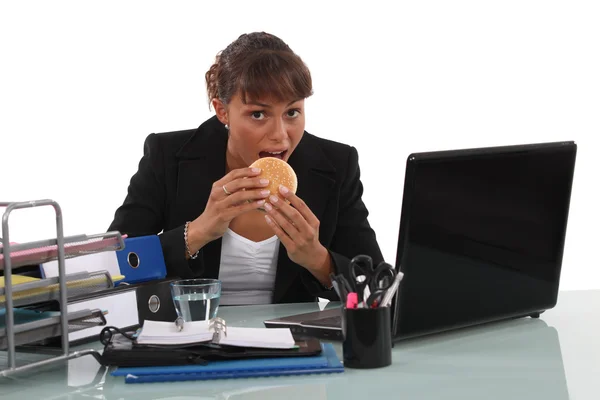 Бизнесвумен ест фаст-фуд за своим столом — стоковое фото
