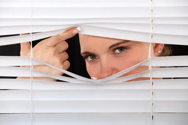 Curious woman peering through window blinds — Stock Photo, Image