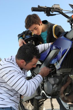 Father and son repairing their motorcycle clipart