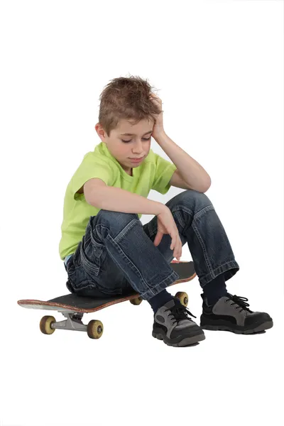 Грустный мальчик сидит на скейтборде — стоковое фото