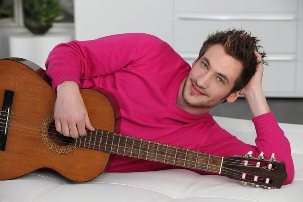 Uomo sdraiato sul divano con chitarra acustica — Foto Stock