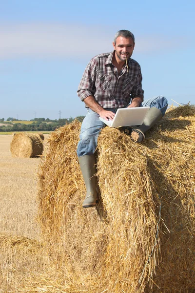 Αγρότης με ένα φορητό υπολογιστή που κάθεται σε μια θυμωνιά χόρτου — Φωτογραφία Αρχείου