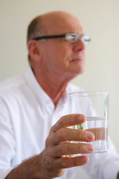 Yaşlı bir adam su ile ilaç alarak — Stok fotoğraf
