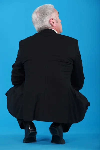 Senior zakenman crouching met terug naar camera — Stockfoto