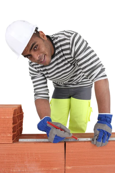 Mixed-race bricklayer taking measurements on brick wall — Stock Photo, Image