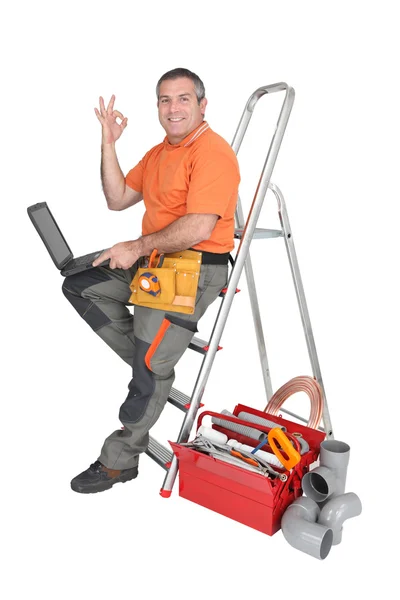 ラップトップ コンピューターを保持している梯子の上に座っていた労働者 — ストック写真