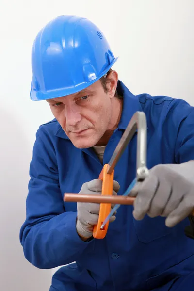 A tradesman using a saw to cut a copper tube — Stock Photo, Image