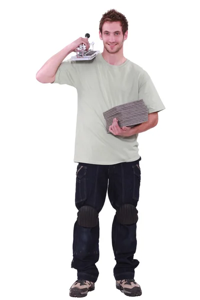 Um jovem segurando telhas e um cortador de telhas — Fotografia de Stock