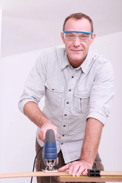 Safety conscious man wearing goggles whilst using electric saw — Stock Photo, Image