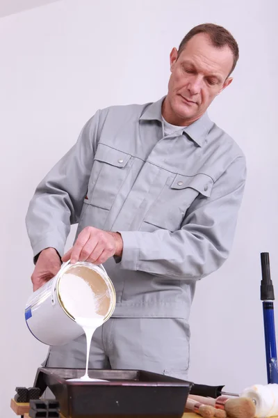 Pintor en el trabajo vertiendo pintura de lata en bandeja —  Fotos de Stock