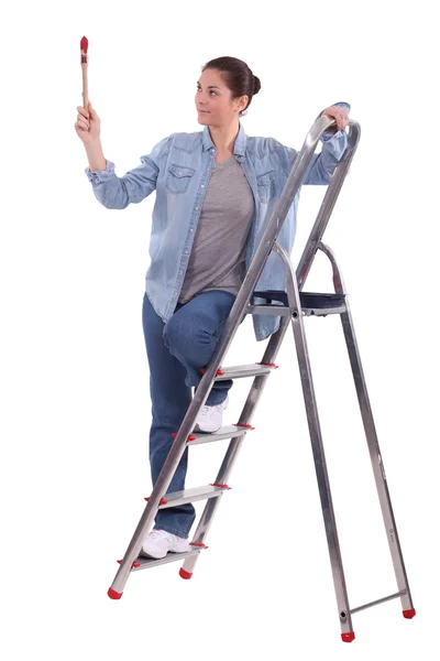 Jonge vrouwelijke schilder op ladder met verhoogde borstel — Stockfoto