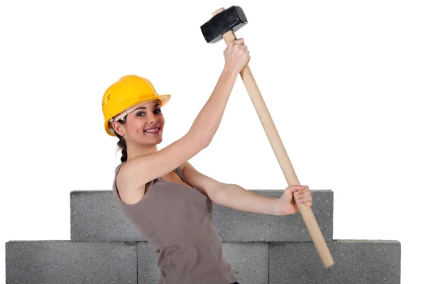 Mulher levantando martelo de trenó na frente da parede inacabada — Fotografia de Stock