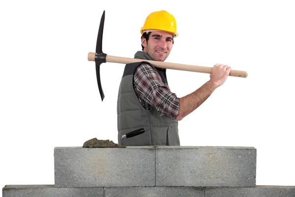 Builder carrying pick-axe stood by wall — Stock Photo, Image