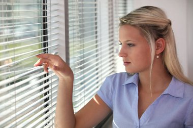 Blond office worker peering through window blinds clipart