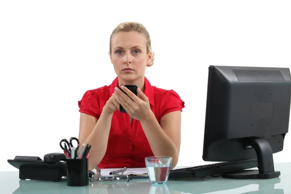 女性は彼女のオフィスの机で携帯電話を使用して — ストック写真