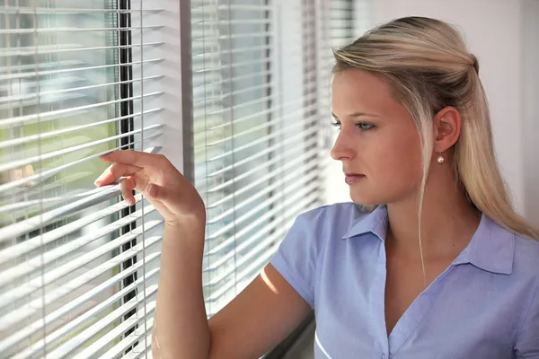 Blond kantoor werknemer "peering" via venster jaloezieën — Stockfoto
