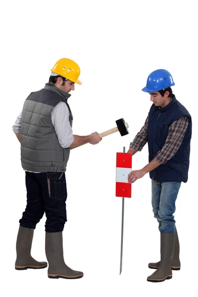 Two workers hammering sign into the ground — Stock Photo, Image