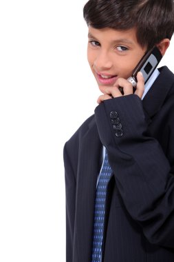 Little boy wearing a business suit and chatting on a cellphone clipart