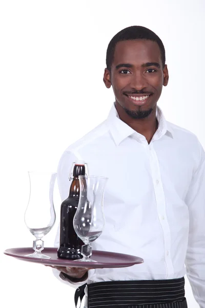 Черный официант несет бутылку пива на подносе — стоковое фото