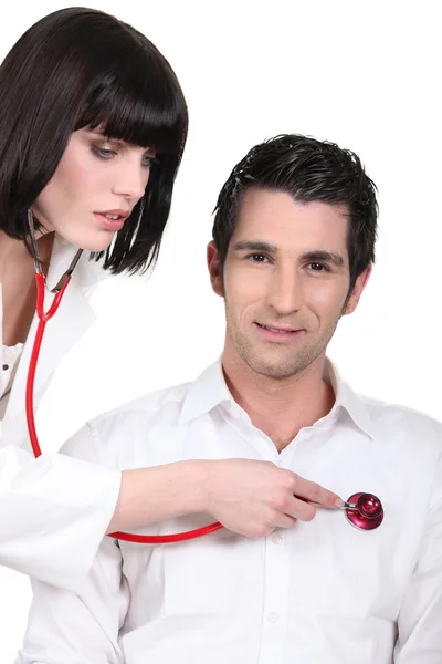 Attraktiva kvinnliga läkare lyssnar på hennes manliga patientens hjärtslag — Stockfoto