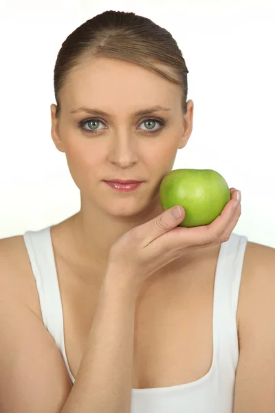 Молодая женщина держит зеленое яблоко на лице — стоковое фото