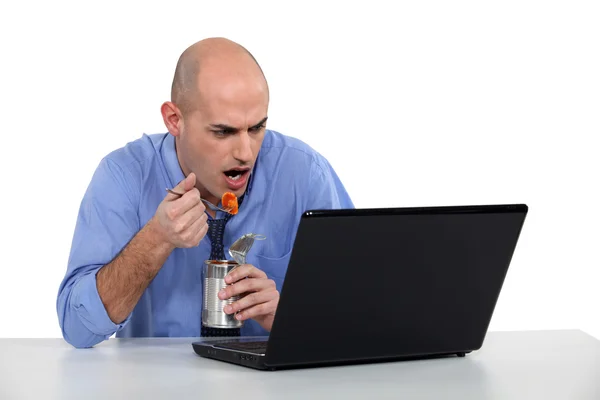 Businessman sat at desk eating from tin can — Stock Photo, Image