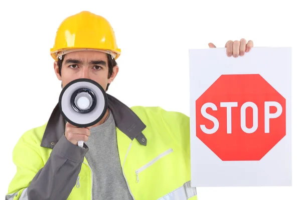 Дорожный рабочий держит знак "стоп" и разговаривает через мегафон — стоковое фото