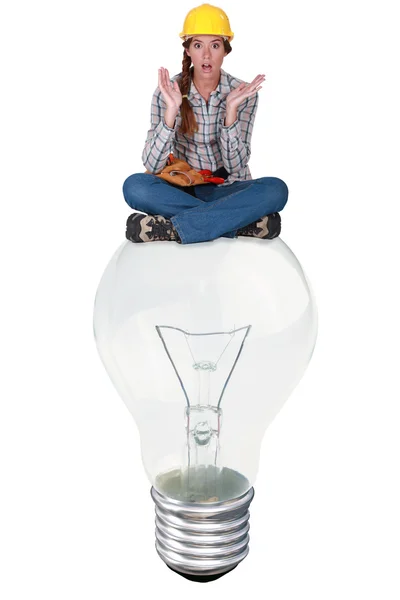 Donna con espressione di sorpresa seduta su una grande lampadina — Foto Stock