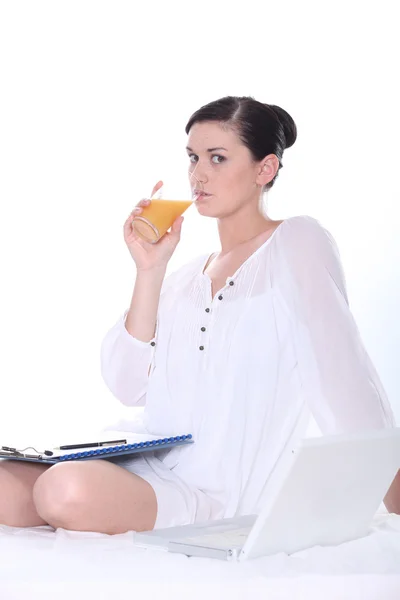 Mujer bebiendo jugo con un portátil y portapapeles — Foto de Stock