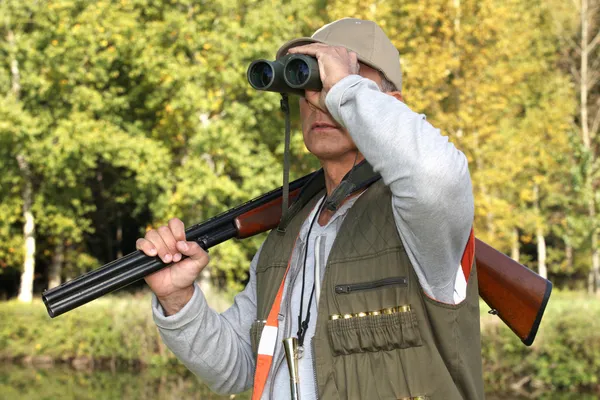 Caçador com rifle olhando através de binóculos — Fotografia de Stock