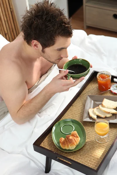 ベッドで朝食を持つ若い男 — ストック写真