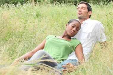 Mixed-race couple relaxing in a field clipart