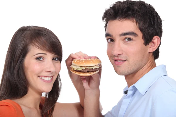 Estúdio de um jovem casal compartilhando um hambúrguer — Fotografia de Stock