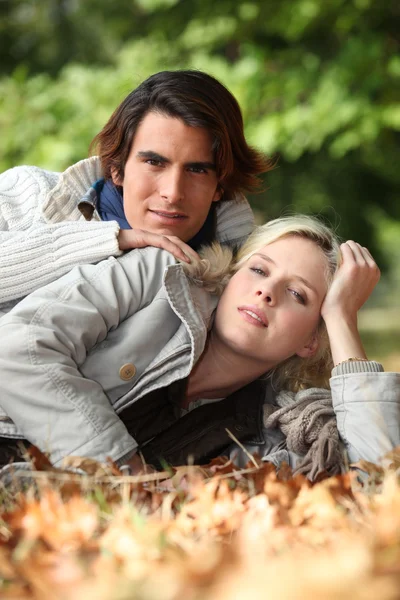 Young couple laying in autumnal leaves — Stock Photo, Image
