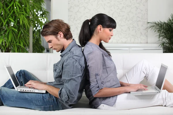 Casal usando dois laptops no sofá — Fotografia de Stock