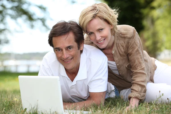 Couple using their laptop in a field — Stock Photo, Image